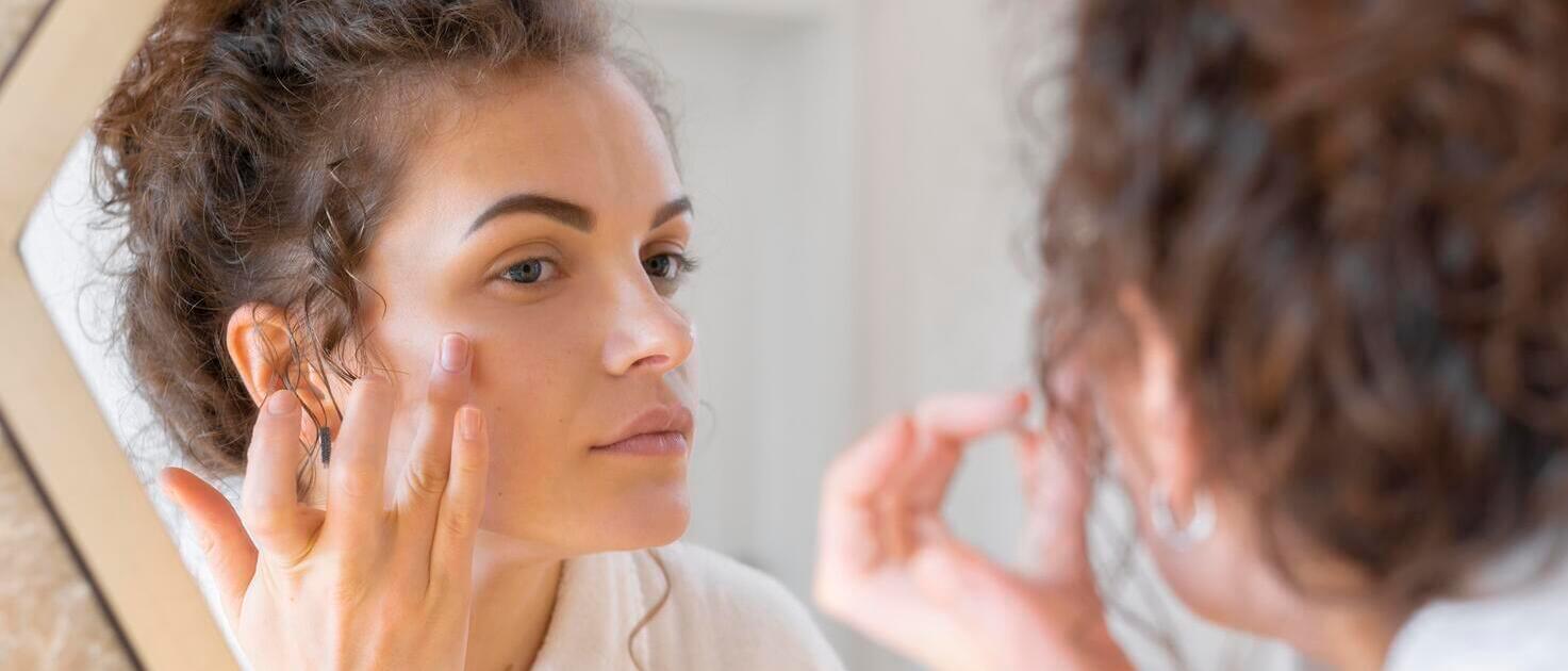 Mulher olhando em espelho enquanto utiliza produto para pele